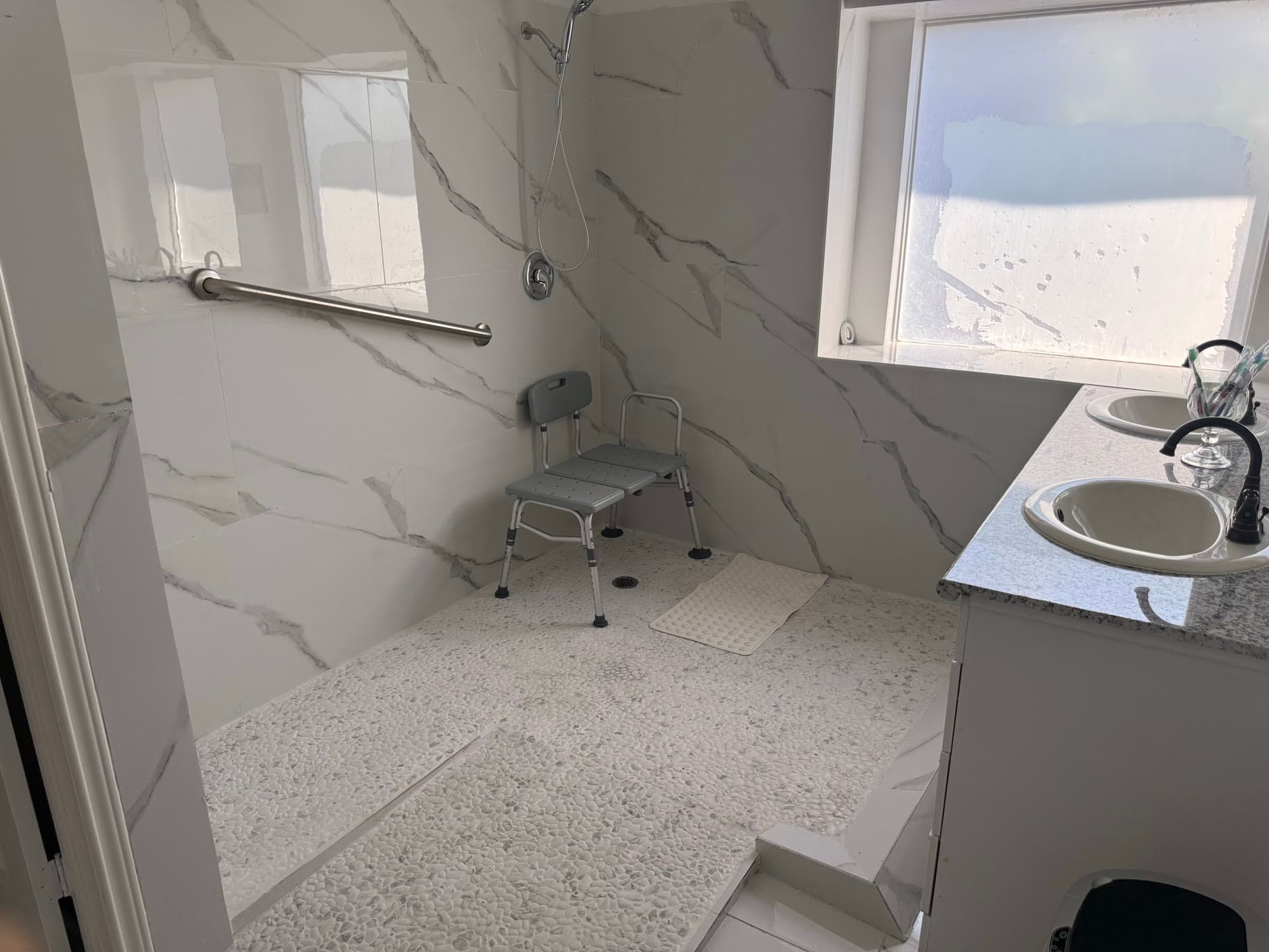 Accessible bathroom with marble walls, grab bars, and shower seat