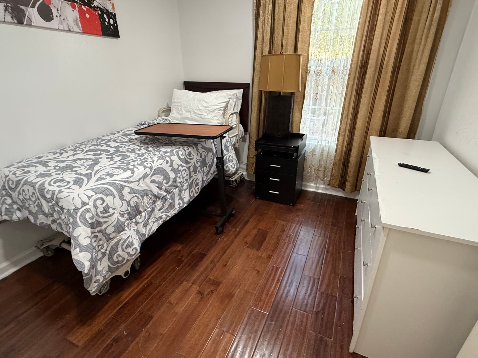 Resident room with patterned bedding, nightstand, and white dresser