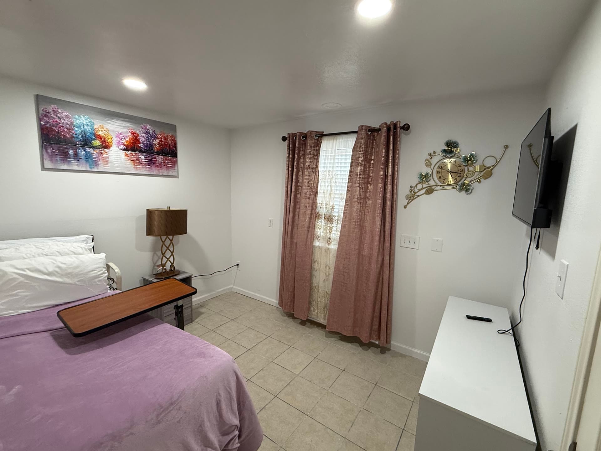 Private room with purple bedspread, colorful tree painting, and pink curtains