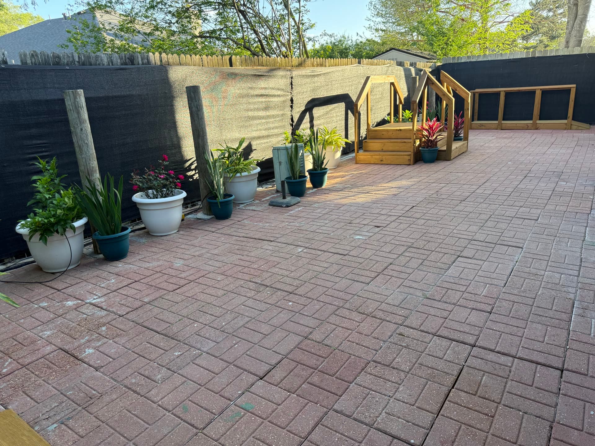 Brick patio with potted plants, privacy fence, and wooden deck stairs